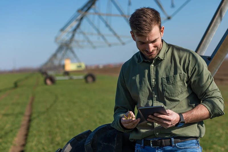 Homme regardant une tablette accoudé à un arroseur agricole